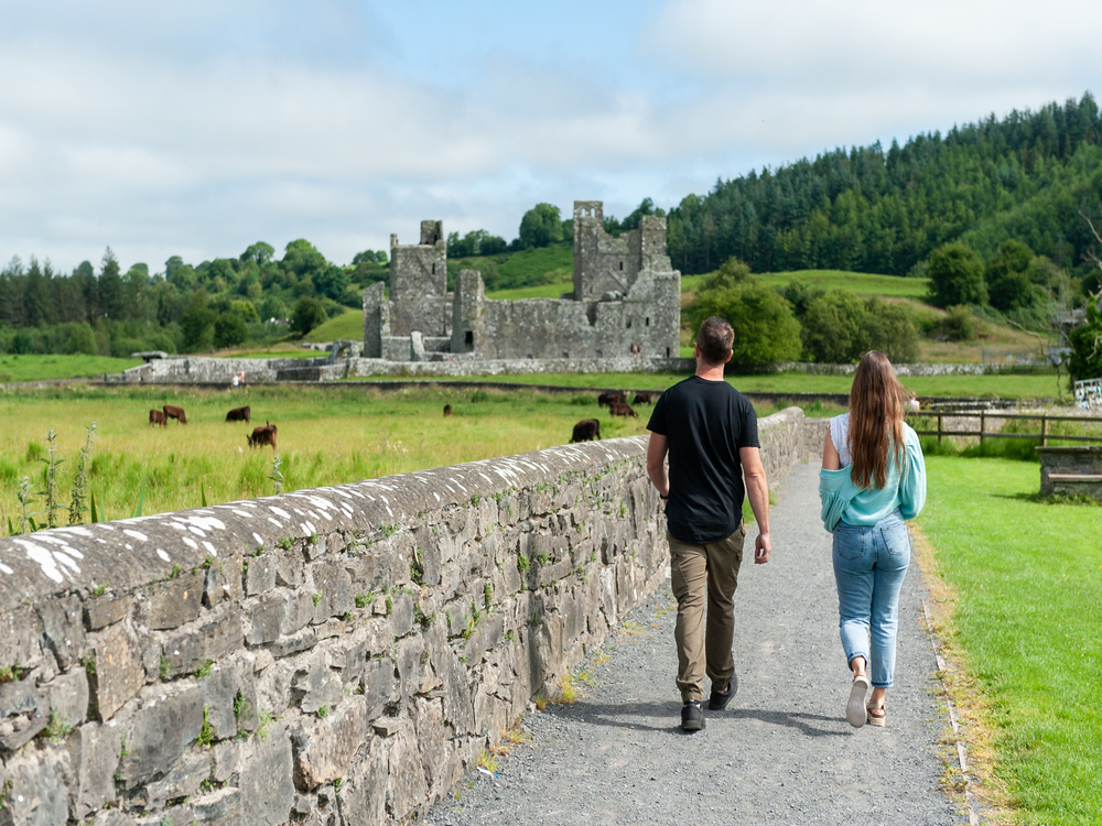Couple Waling on a gravel track beside a stone wall and green grass